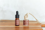 Two bottles of Autumn Essential Oil Blend with cinnamon pumpkin scent, one larger and one smaller, both with dropper caps, placed on a wooden surface.