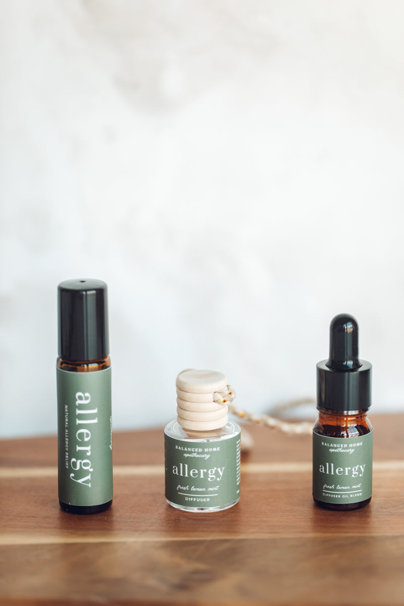 Three bottles of essential oil blend labeled 'Allergy', including a rollerball and two diffuser oil bottles, displayed on a wooden surface.