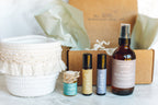 Collection of natural health products including bottles and containers on a light surface with a blurred background. balanced home apothecary best sellers bundle that includes a white basket, calm hanging car diffuser, joyful rollerball, sleep rollerball, and hormones magnesium spray, with a brown box, mint tissue paper, and beige nest.
