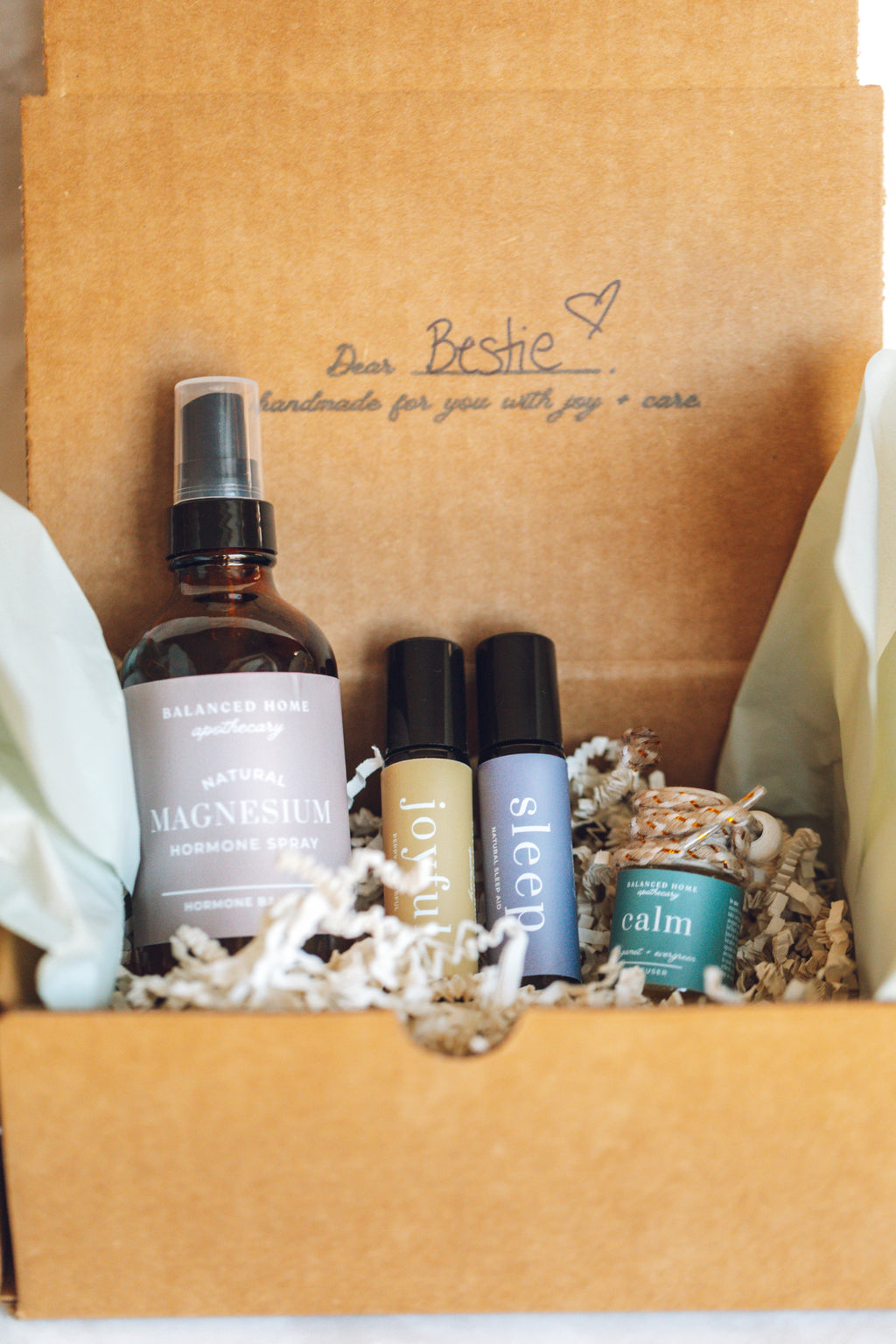 balanced home apothecary best sellers bundle that includes a white basket, calm hanging car diffuser, joyful rollerball, sleep rollerball, and hormones magnesium spray, with a brown box, mint tissue paper, and beige nest.