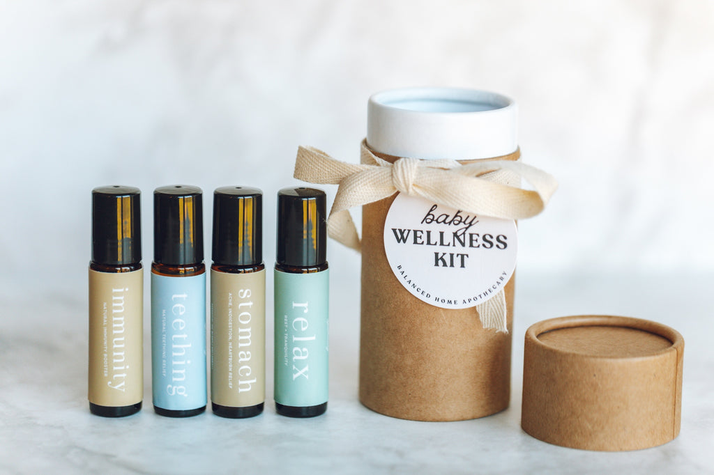 Baby wellness kit with bottles and a cylindrical container on a white background, kit includes immunity boosting essential oil rollerball, teething relief essential oil rollerball, stomach essential oil rollerball, and relax essential oil blend rollerball.
